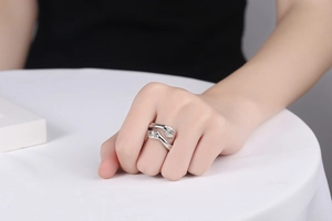 Close-up of silver hugging hands open ring worn by a model against black clothing
