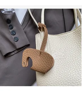 Detail of elephant-shaped caramel pebbled leather charm hanging on a cream tote bag handle