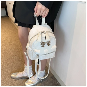 Detail of white mini backpack with gold bow accent and fine matte texture
