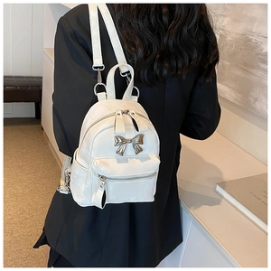 Detail view of white mini backpack with silver metal bow and adjustable straps on model
