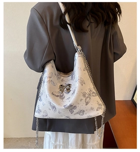 Close-up of white glossy tote bag with butterfly prints and metal bow detail