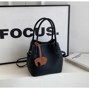 Detail of black lychee grain bucket bag with white stitching and cute elephant charm