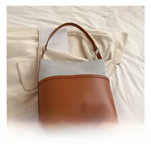Detail of two-tone bucket bag with grey tweed texture and brown leather base on fabric