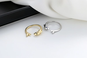 Detail view of gold and silver shark open rings with blue gemstone eyes on fabric