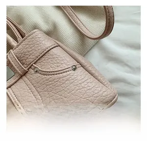 Close-up of litchi texture leather stitching and metal buckle details on a pink handbag