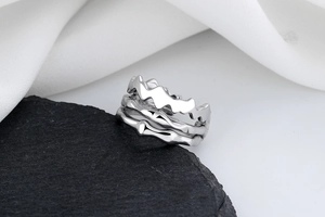 Close-up of a silver irregular wavy ring placed on a black rock with silk background