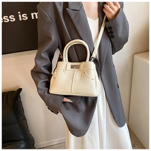 Close-up of cream textured faux leather handbag with denim pocket design and metal lock