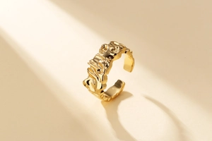 Détail d'une bague dorée avec texture de lave irrégulière et anneau ouvert ajustable