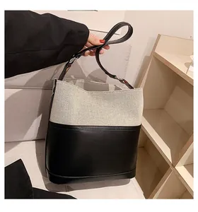 Detail of beige canvas and black leather bucket bag with top handle and spacious design