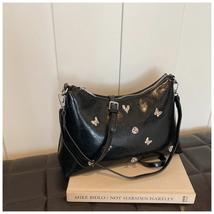 Détail d'un sac à bandoulière noir brillant avec breloques papillon en métal argenté