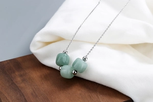 Macro shot of S925 silver necklace with three light green Hetian jade beads on wood