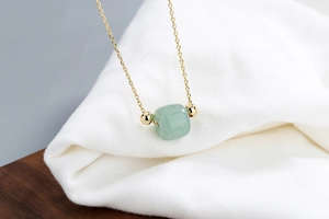 Macro shot of Hetian jade pendant necklace with gold beads on white knit fabric