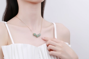 Close-up of golden necklace with three green jade-like beads on a model's neck
