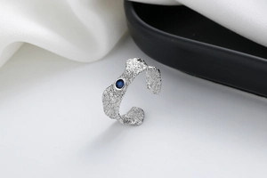 Macro detail of silver textured ring with a deep blue zircon and irregular hammered finish