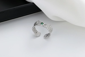 Detail of silver textured ring with green zircon on white silk and geometric blocks
