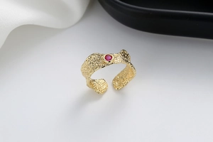 Detail of gold open ring with lava texture and a sparkling red round zircon stone