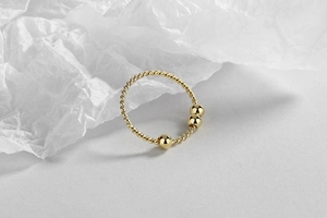 Detail shot of golden twisted ring band featuring three polished beads on white background