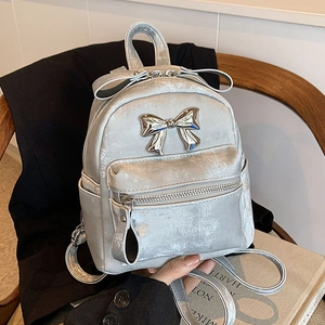 Silver mini backpack with metallic finish and bow accent on a wooden chair