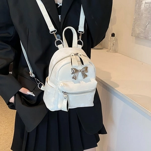 Chic white mini backpack with metal bow detail worn over a black blazer for daily style
