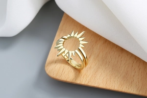 Dettaglio anello dorato a girasole su supporto di legno con seta bianca