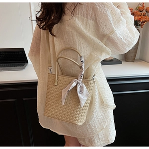 Detail of beige woven bucket bag with floral scarf accessory worn by a model