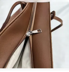 Detail of silver zipper closure and herringbone fabric lining on a brown leather tote bag