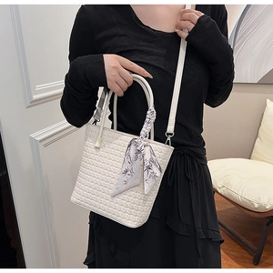 Detail of white woven bucket bag featuring floral scarf handle and adjustable strap