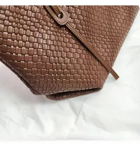 Close-up of brown woven tote bag with checkered texture and decorative metal rivets