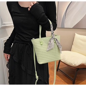 Close-up of light green woven bucket bag with elegant floral scarf on the handle