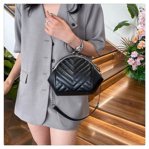 Detail of black quilted shell bag with silver round handle and metallic chain strap