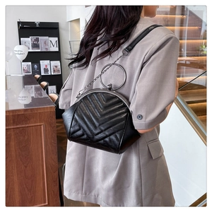 Detail of black quilted shell bag with V-shaped stitching and metal ring handle