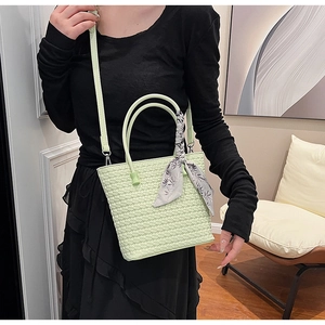 Detail of light green woven bucket bag with decorative silk scarf on the handle