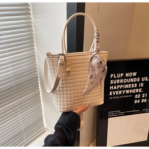 Detailed view of white woven bucket bag featuring a floral silk scarf on the handle
