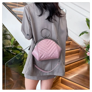 Detail of pink chevron quilted shell bag with round metal handle and chain strap on model