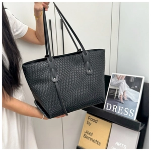 Detail of a black woven leather tote bag with a diamond pattern and thin straps