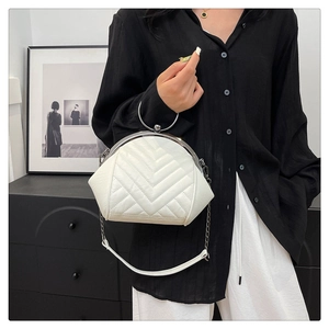 Detail of white quilted V-stitch shell bag with silver round metal handle and chain strap