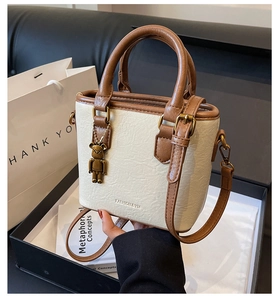 Détail d'un sac seau blanc avec poignées marron et breloque ours dans une boîte cadeau