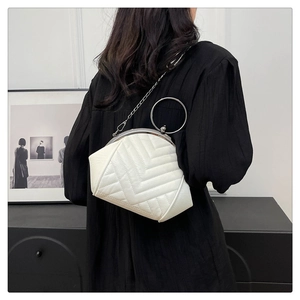 Close-up of white quilted handbag with silver ring handle and chain strap on model