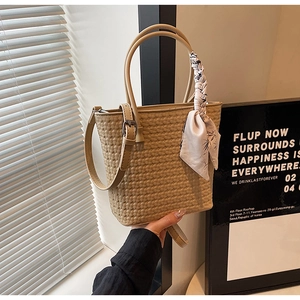Detail of beige woven bucket bag featuring silk scarf decoration and adjustable strap