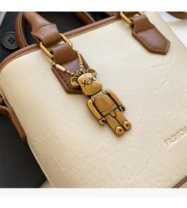 Gros plan du sac seau en cuir litchi blanc cassé avec pendentif ours et gaufrage fashion