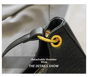 Détail de l'œillet doré et de la bandoulière amovible sur un sac noir à motif crocodile