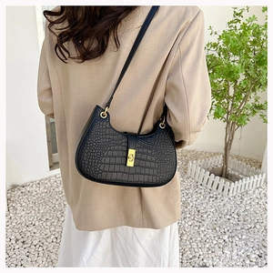 Modèle portant un sac hobo noir à motif crocodile avec fermoir doré et tenue minimaliste