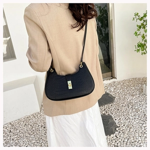 Détail d'un sac noir motif crocodile avec boucle dorée sur une tenue blazer beige