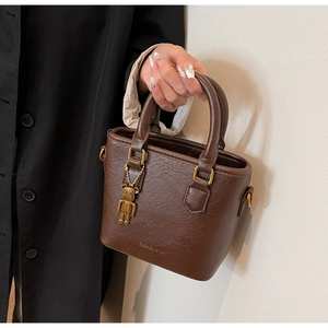 Détail du mini sac marron foncé avec poignée ronde dorée et pendentif ours style KAWS