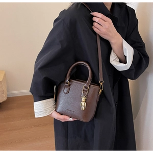 Détail d'un sac seau en cuir marron texturé avec un pendentif ours doré sur le côté