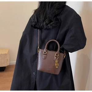 Détail du mini sac seau en cuir marron foncé avec ornements dorés et breloque ours