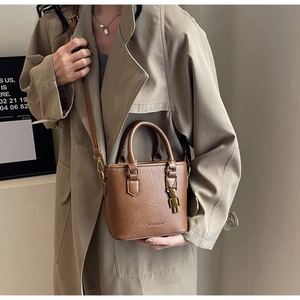 Sac seau en cuir caramel avec charm d'ours porté sur un trench-coat classique beige