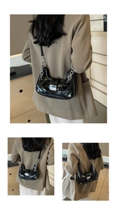 Detail of a black patent leather crescent bag featuring silver chain and metal clasp