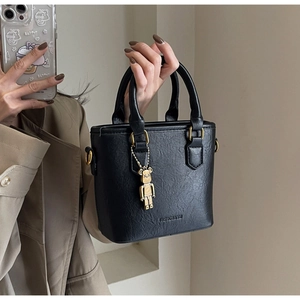 Détail d'un sac seau noir avec texture plissée, poignée dorée et breloque ours