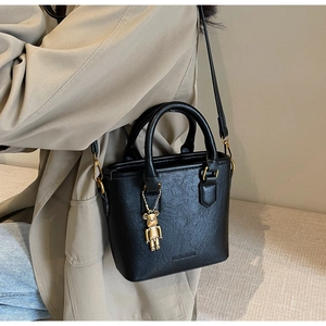 Détail d'un sac cabas noir en PU à texture plissée avec pendentif ours doré sur fond de manteau